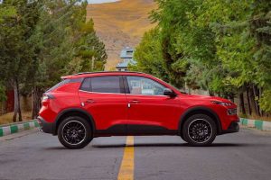 ماشین ریرا به رنگ قرمز از نمای جانبی پارک‌شده روی آسفالت با درخت‌کاری در دو طرف جاده