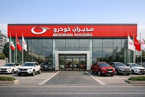 نمای بیرونی یک نمایندگی مدیران خودرو با تابلو نمایندگی قرمز و ماشین‌های پارک شده