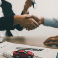 نمایی از توافق مالی برای خرید خودرو با وام، همراه با اسناد قرارداد و ماکت خودرو روی میز