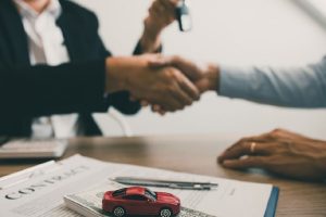 نمایی از توافق مالی برای خرید خودرو با وام، همراه با اسناد قرارداد و ماکت خودرو روی میز