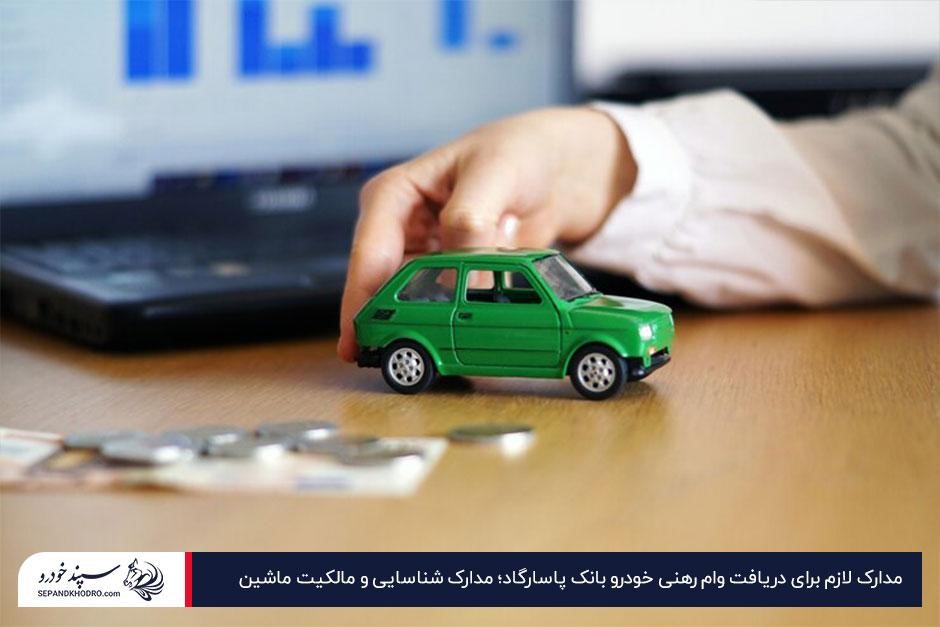تصویر میز کار با یک ماشین اسباببازی سبز، چند سکه و لپتاپ در پسزمینه