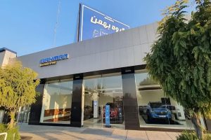 عکس نمایندگی بهمن موتور تهران با تابلو آبی بزرگ و خودرو آبی پارک‌شده در سالن